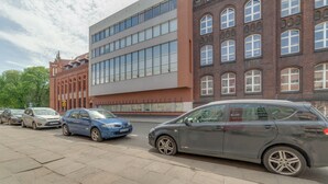 A parking lot with several cars parked in front of a building with a red brick facade and large windows. - Dream Loft Łagiewniki (Gdansk)