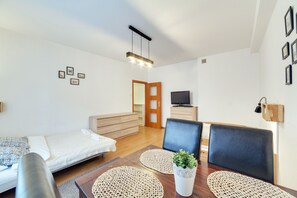 A modern, well-lit room with a bed, two chairs, a dining table, and a TV.