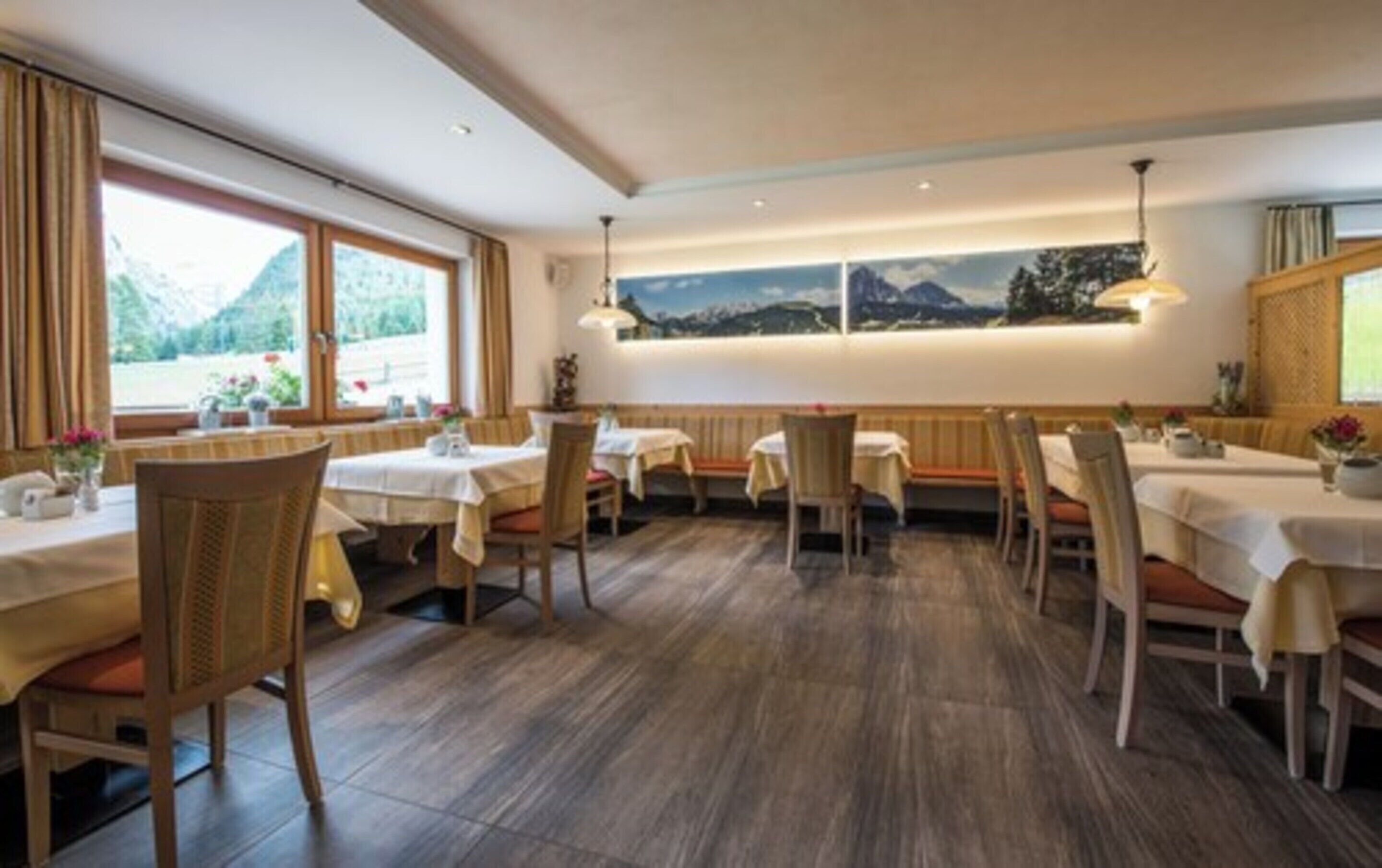 Un restaurant amb taules i caires de fusta, un gran finestral amb vista a la muntanya i un mural a la paret.