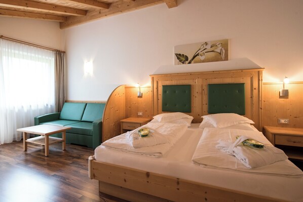Una cama de madera con ropa de cama blanca, una mesita de noche de madera, un sofá verde y una mesa de madera.