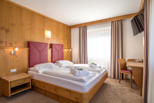 A wooden-paneled room with a bed, bedside tables, a desk, and a TV. - Hotel Bel Vert (Selva di Val Gardena)
