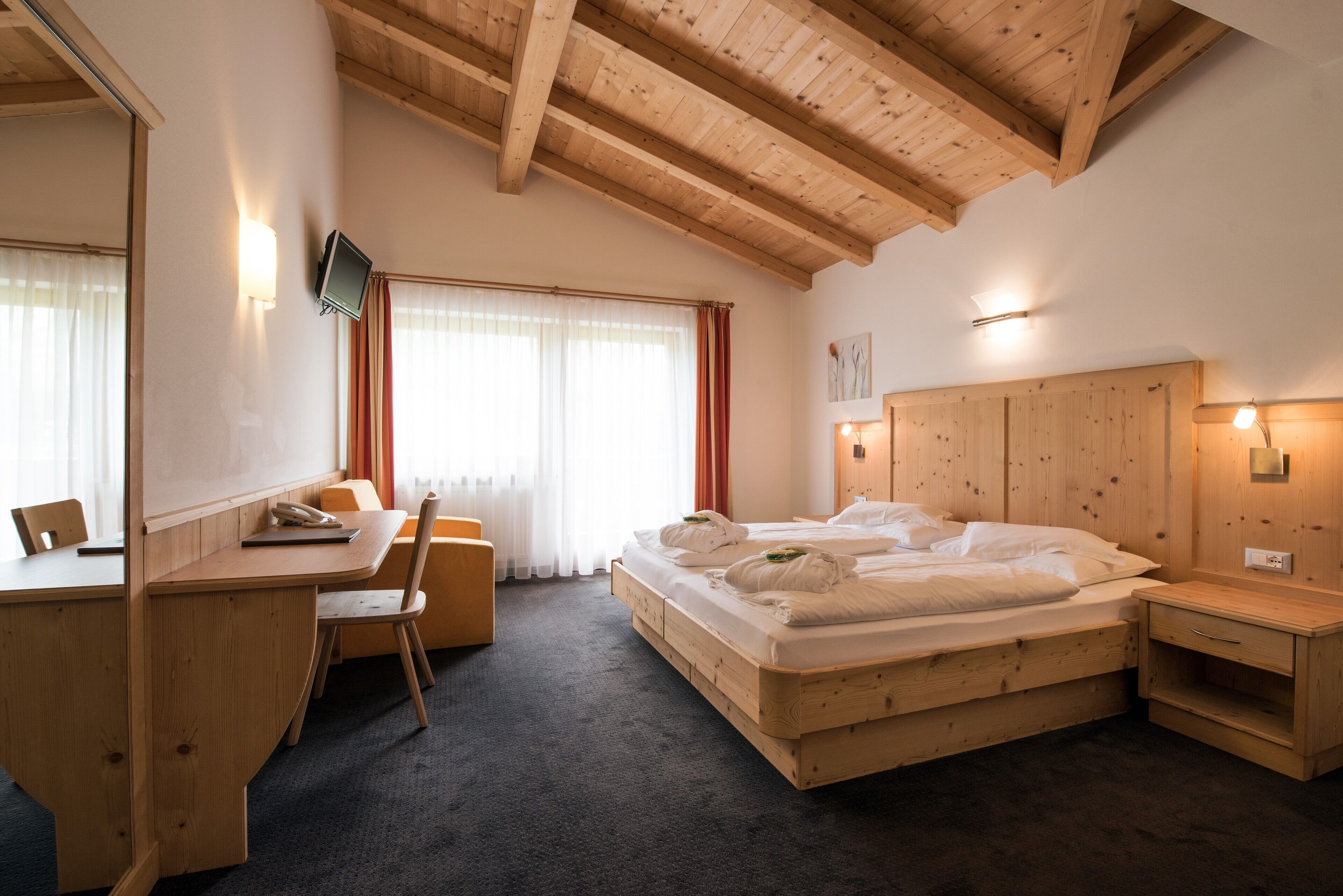 A wooden-framed bedroom with a bed, desk, chair, and bedside table.