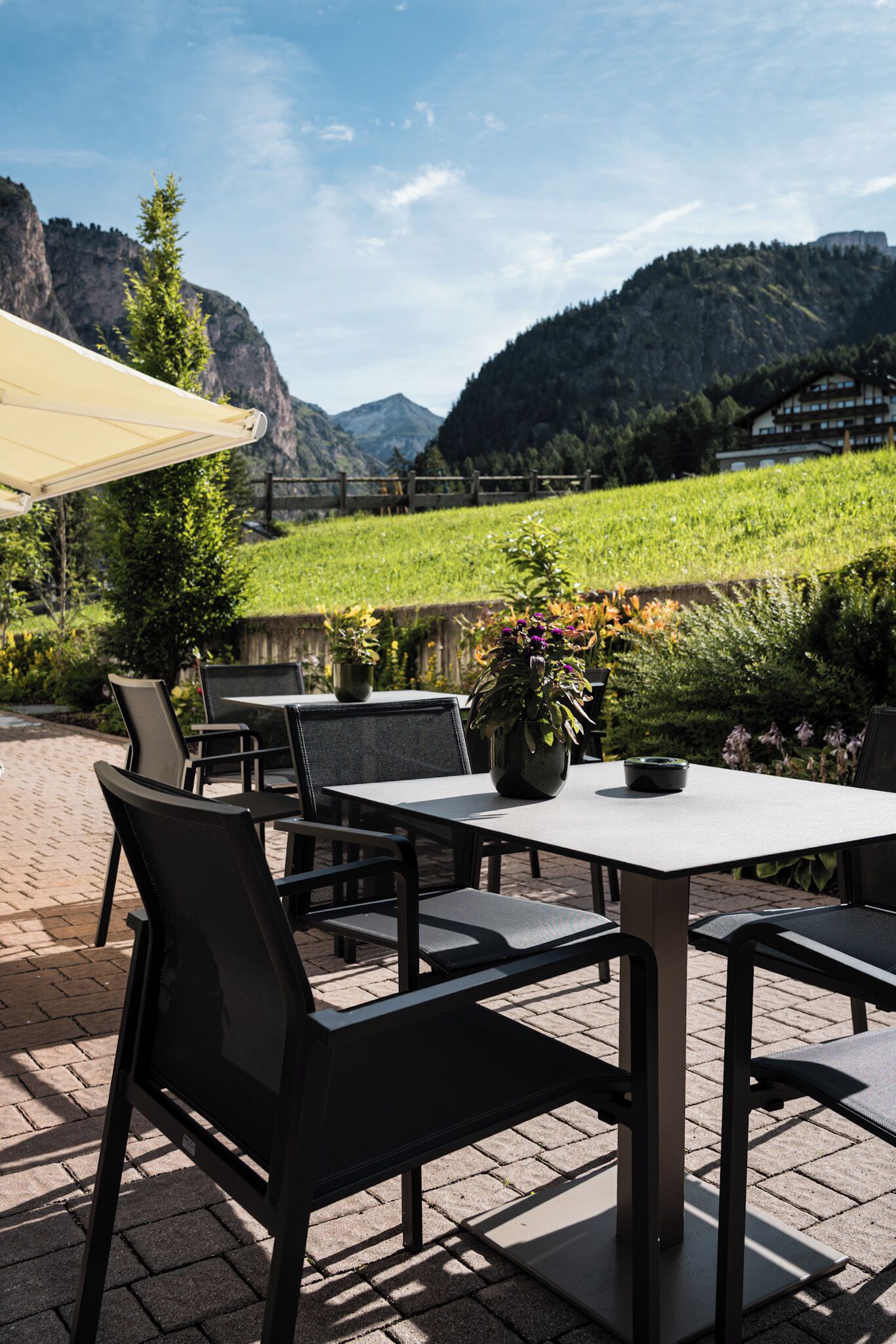 Un patio al aire libre con mesas y sillas, una planta en maceta y vistas a montañas y vegetación.