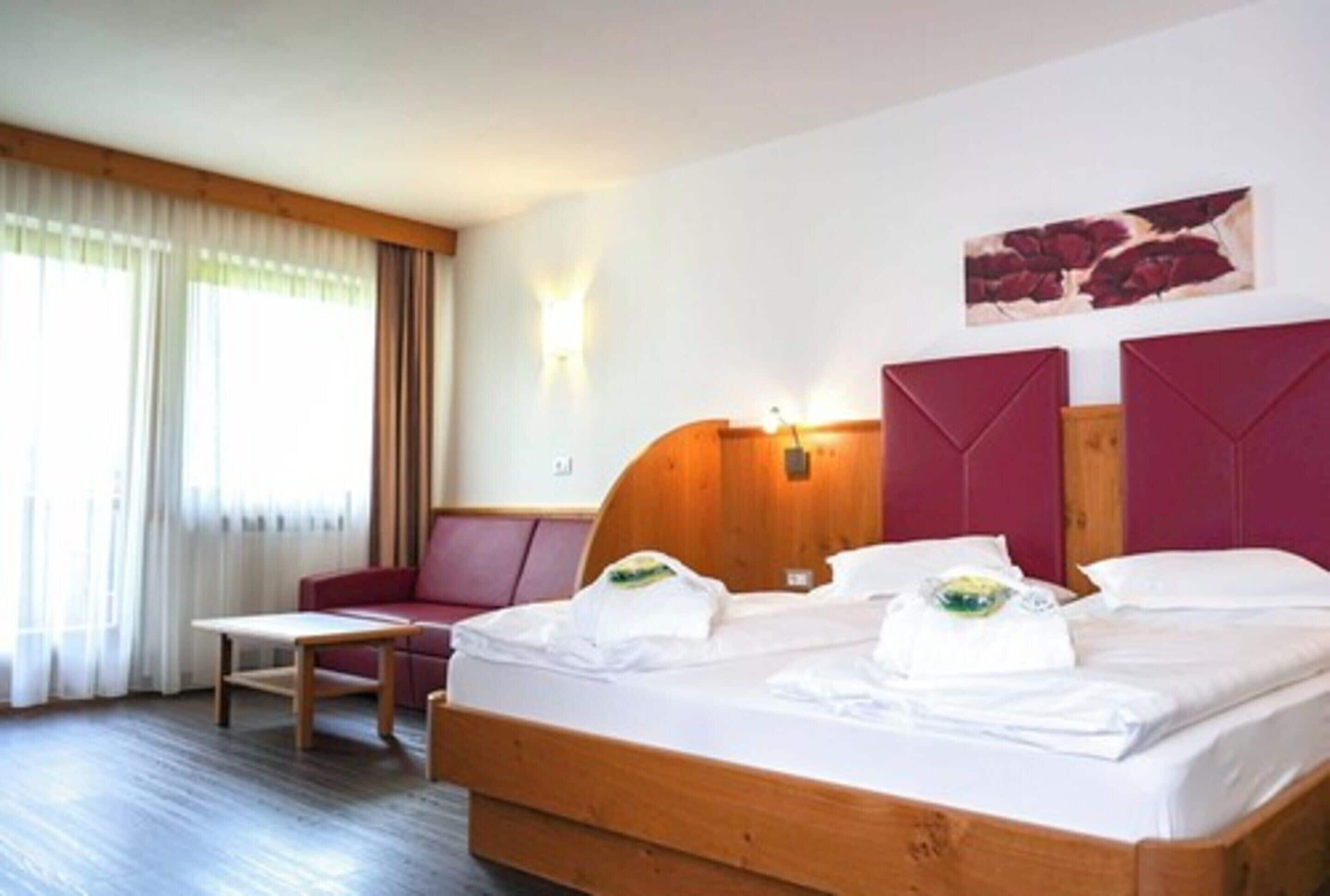 Een hotelkamer met een houten bed, een rode bank, een tafeltje en een schilderij aan de muur.