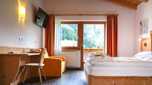 A room with a bed, a desk, a chair, a TV mounted on the wall, and a window with curtains. - Hotel Bel Vert (Selva di Val Gardena)