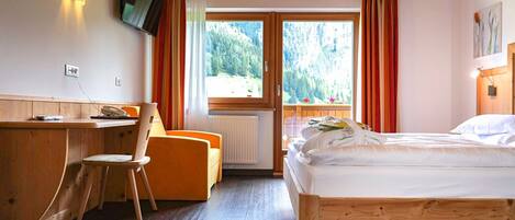 A room with a bed, a desk, a chair, a TV mounted on the wall, and a window with curtains.
