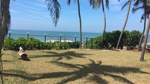 A grassy area with a fence, palm trees, and a view of the ocean. - Ayana Beach Resort (Negombo)