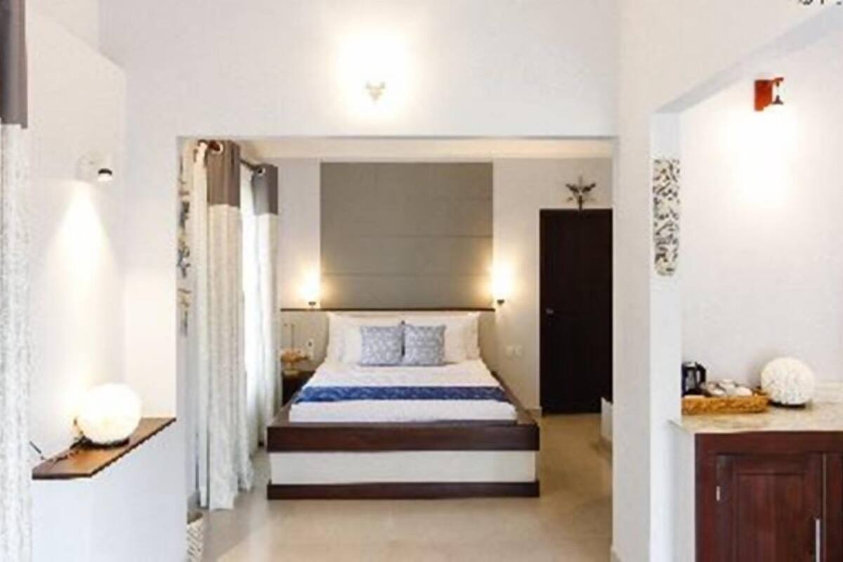 A bedroom with a bed, bedside lamps, a nightstand, and a view into another room.