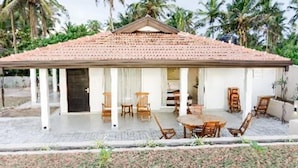 A bungalow with a tiled roof, a covered porch with wooden furniture, and a garden area. - Ayana Beach Resort (Negombo)