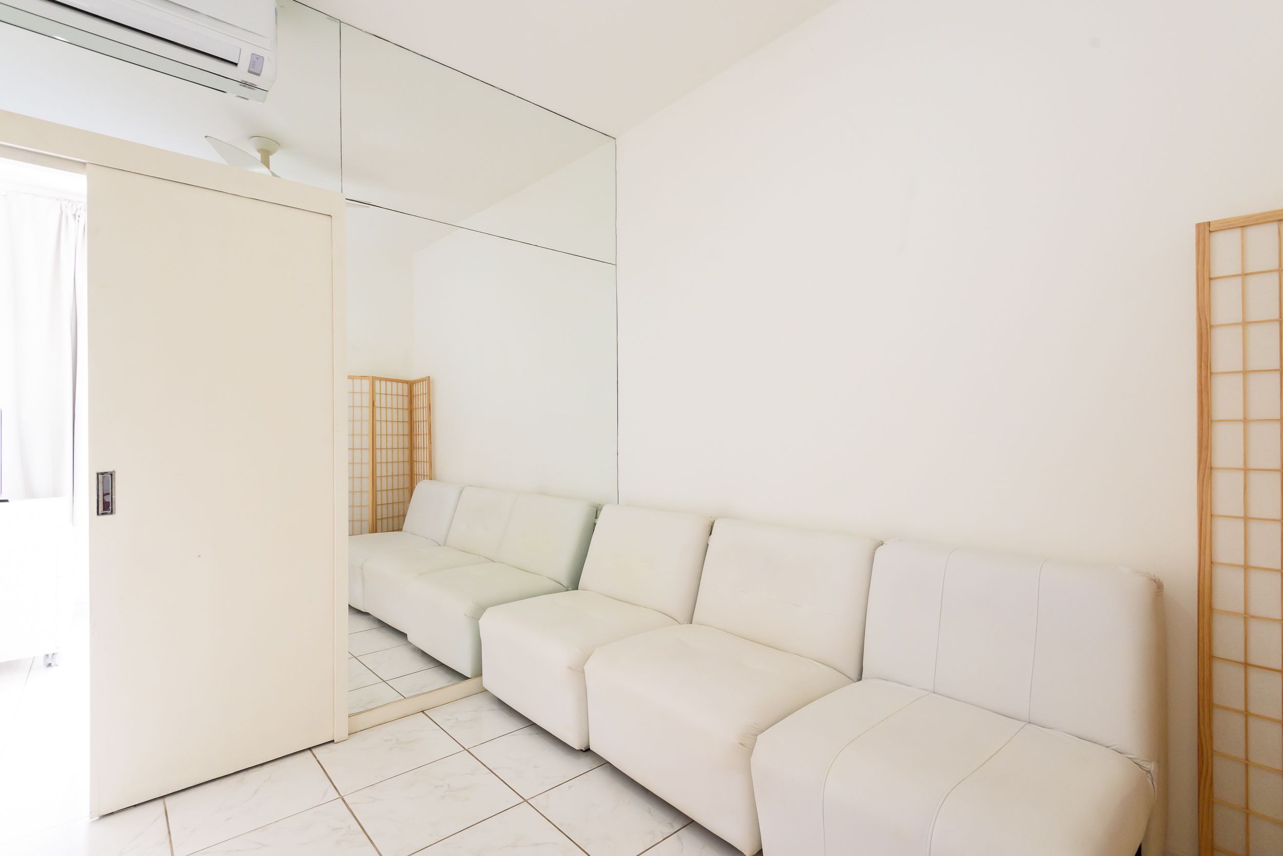 A modern room with a white sofa, a wooden screen, and a tiled floor.