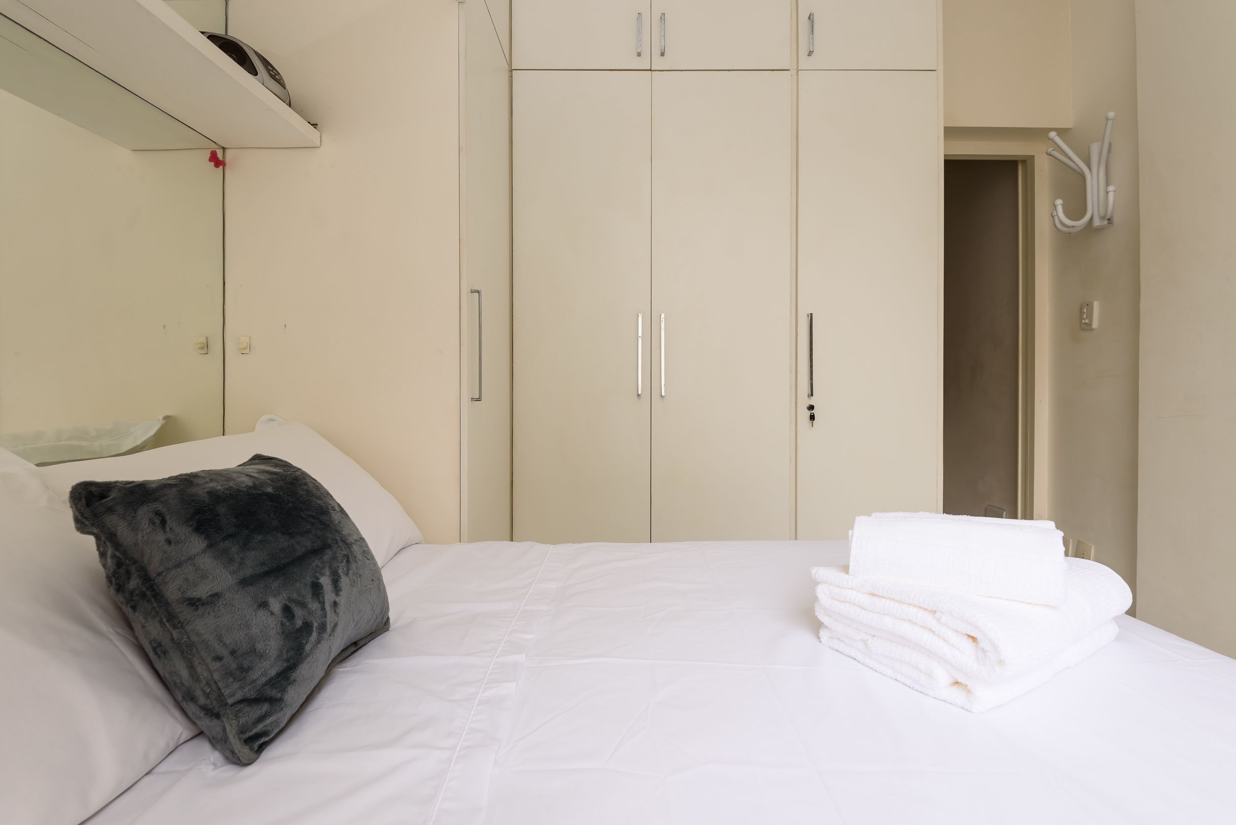 A bedroom with a bed, a dark grey pillow, white towels, and a wardrobe with two doors.