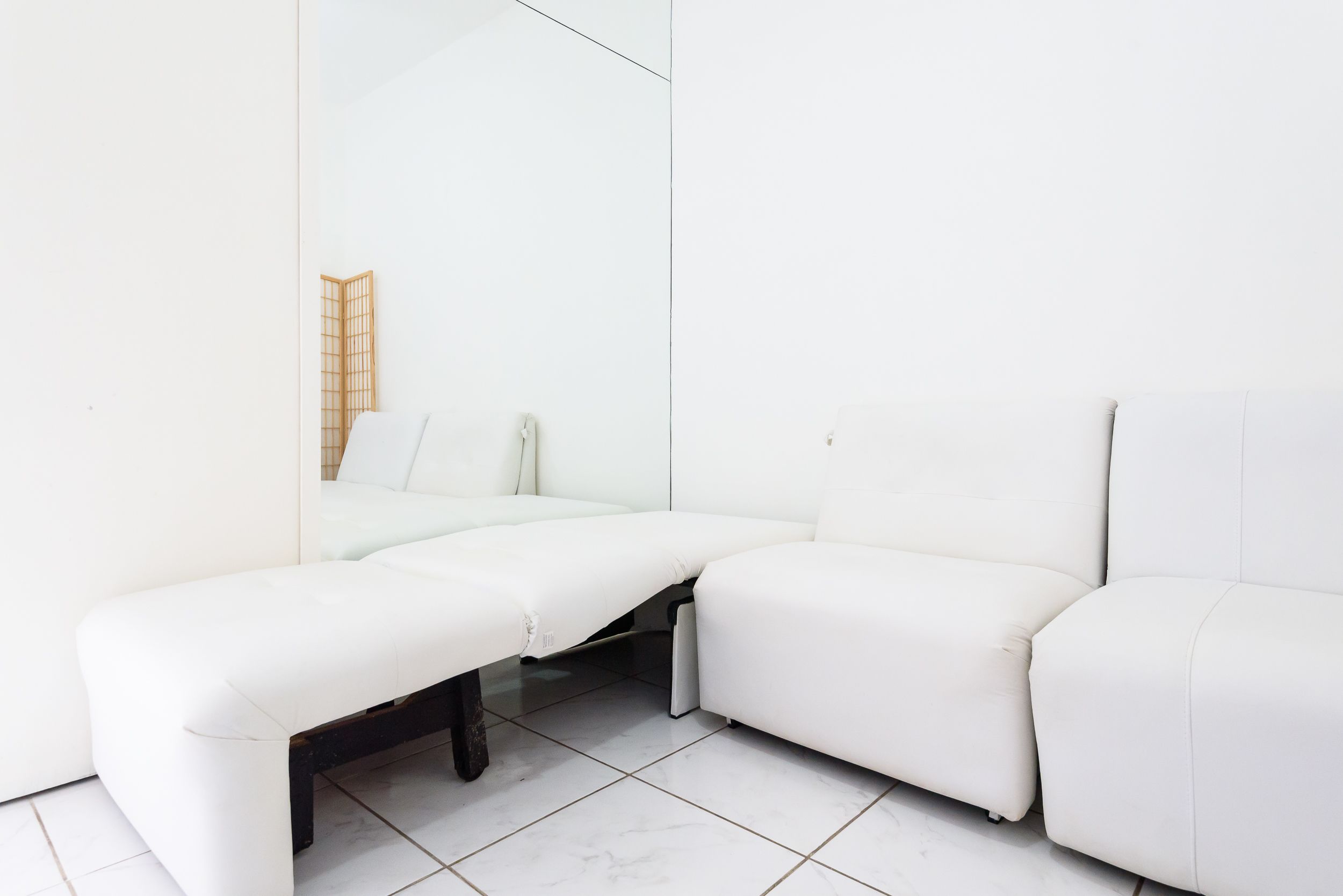 Un sofá blanco con un banco en una habitación minimalista con paredes blancas y suelo de baldosas.