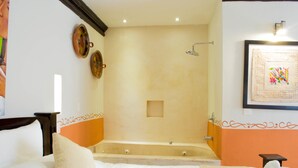 Habitación de hotel con una bañera grande, cama con ropa blanca y zona de ducha.