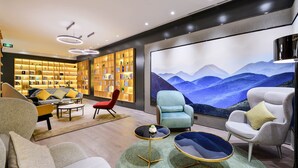 A modern hotel lobby with a large bookshelf, comfortable seating, and a scenic wall mural. - Atour Hotel Hongpailou Chengdu (Chengdu)
