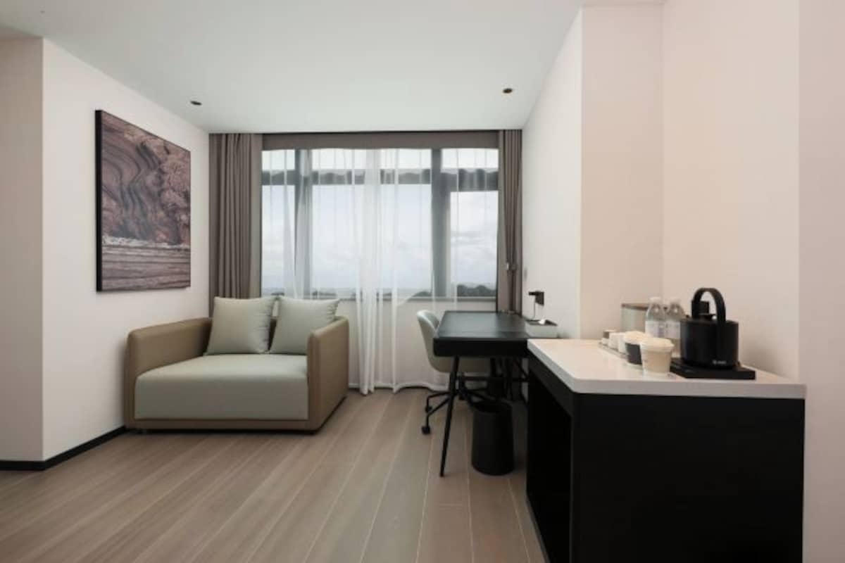 A modern hotel room with a sofa, a desk, and a large window with curtains.
