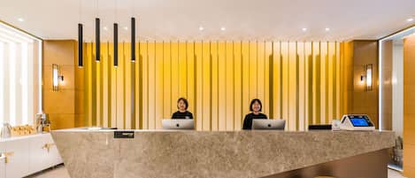 A modern reception desk with two staff members, a marble counter, and a priority club sign.