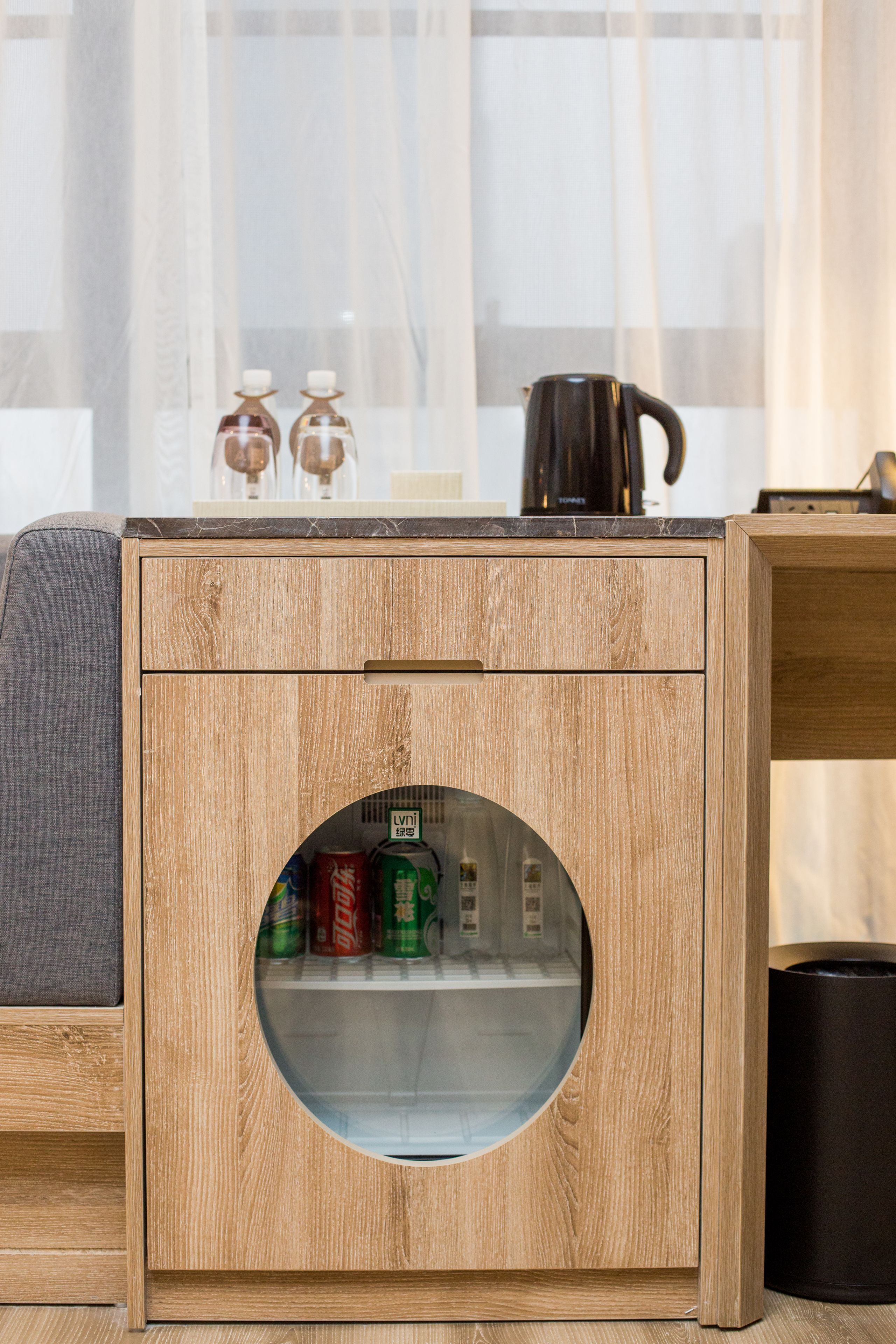 A wooden cabinet with a circular glass door, containing cans and a bottle.