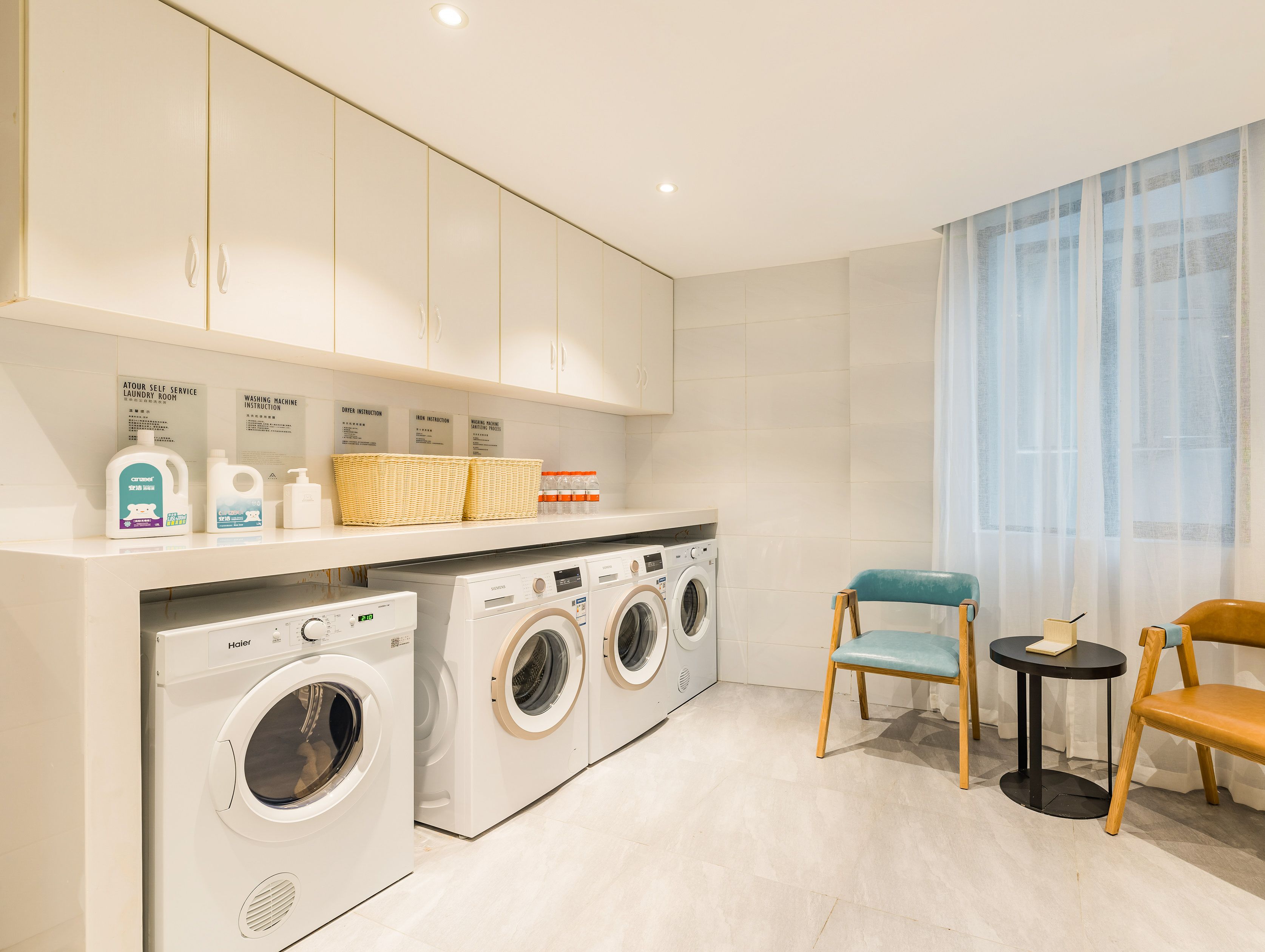 A modern laundry room with a washing machine, dryer, and a small table with a chair.