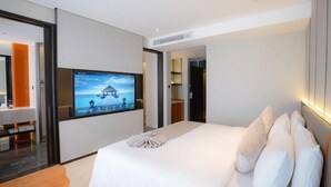Ein modernes Hotelzimmer mit einem großen Bett, einem flachbildfernseher an der Wand und Blick auf einen Strand durch das Fenster.