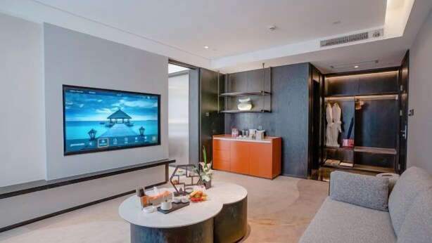 Eine moderne Hotelhalle mit großem Flachbildfernseher, rundem Couchtisch, einer Sitzecke und einer Rezeption sowie einem Bereich zur Kleideraufbewahrung.