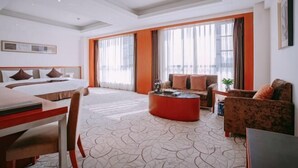 Ein Hotelzimmer mit einem Bett, einem Schreibtisch, einer Couch, einem Couchtisch und großen Fenstern mit Vorhängen.