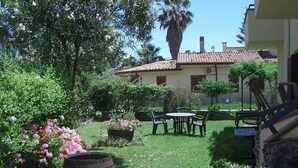 A patio with a table and chairs, surrounded by lush greenery and flowering plants. - Sybaris B&B (Cassano allo Ionio)