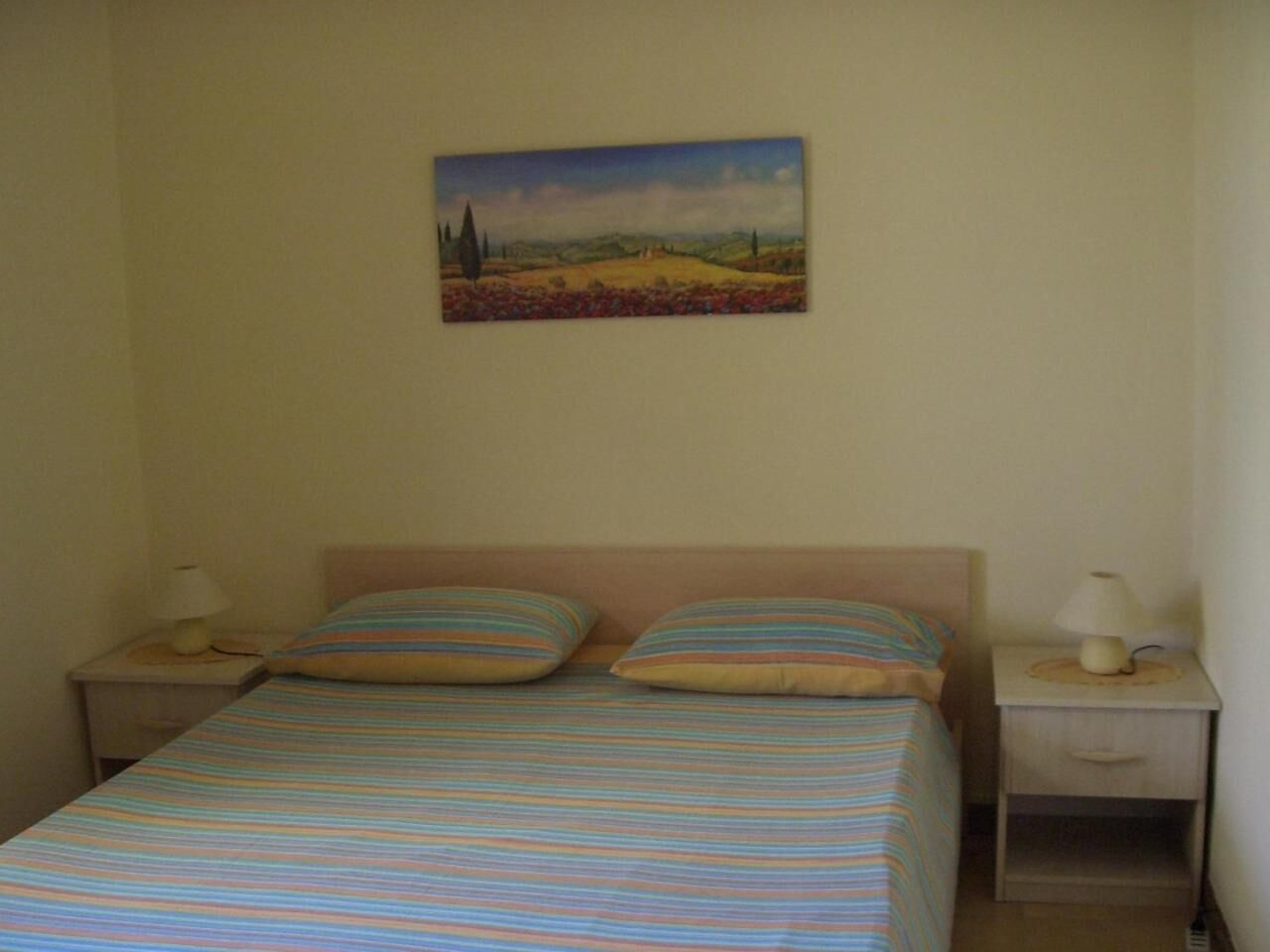 A bedroom with a bed, two pillows, two bedside tables with lamps, and a painting on the wall.