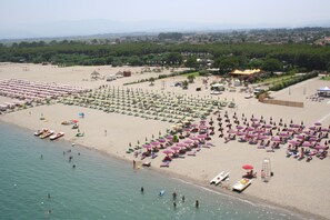 Una spiaggia con file di ombrelloni e lettini, una riva sabbiosa e barche in acqua.