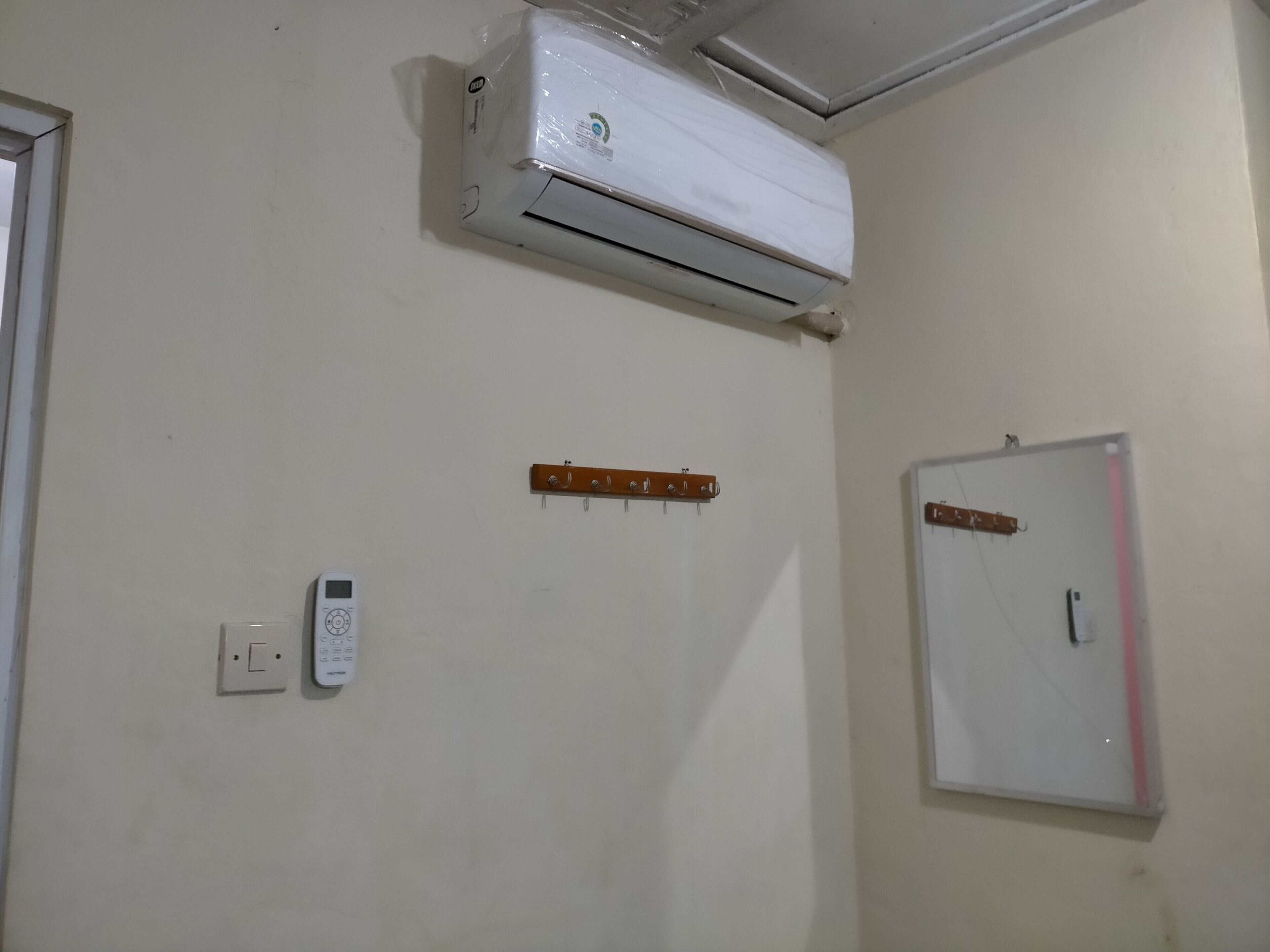 Una habitación con un equipo de aire acondicionado blanco fijado a la pared, un cuadro eléctrico en la pared y una pizarra con una franja rosa.