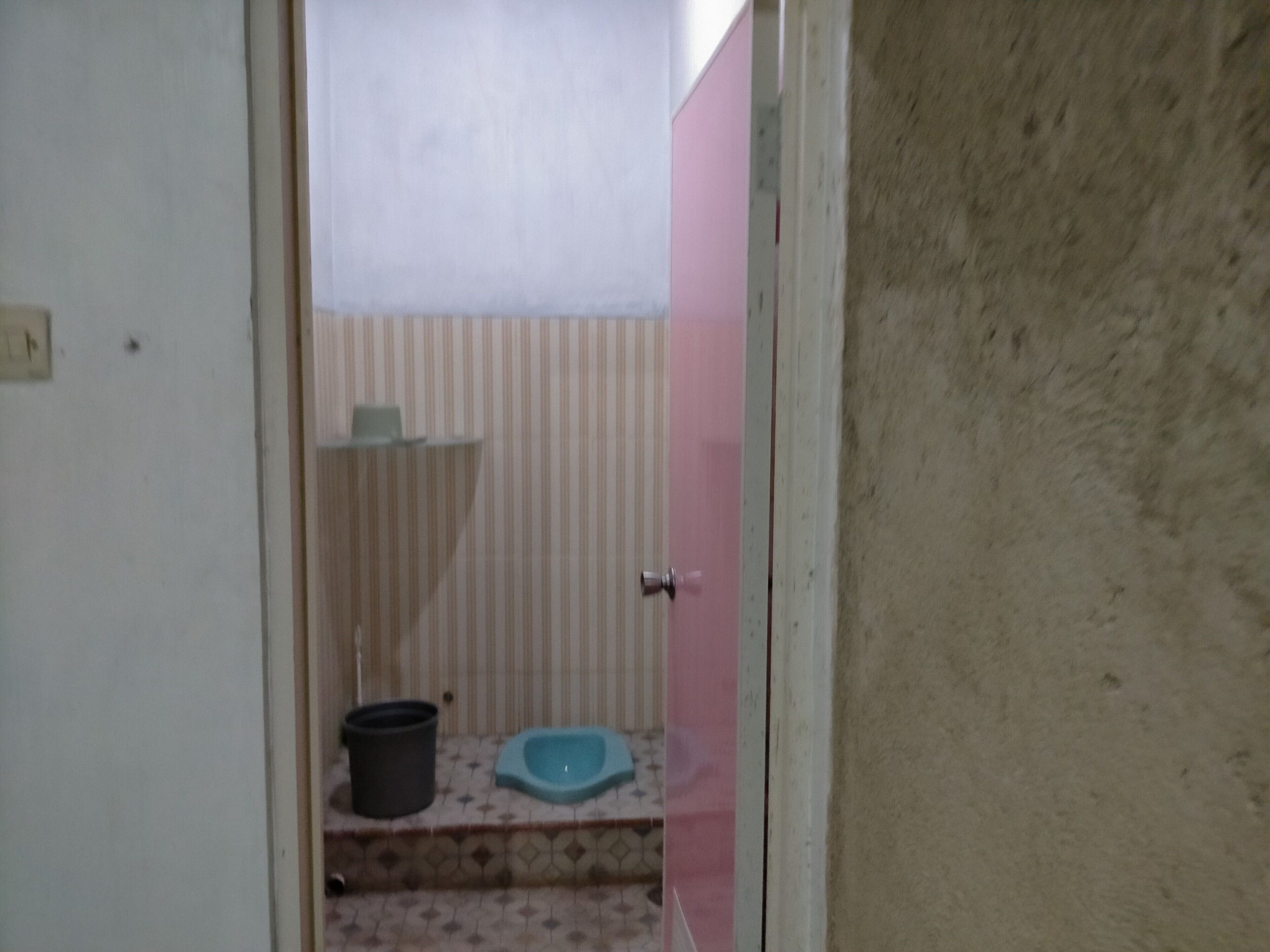 A small bathroom with a toilet, a trash bin, and a blue bidet.