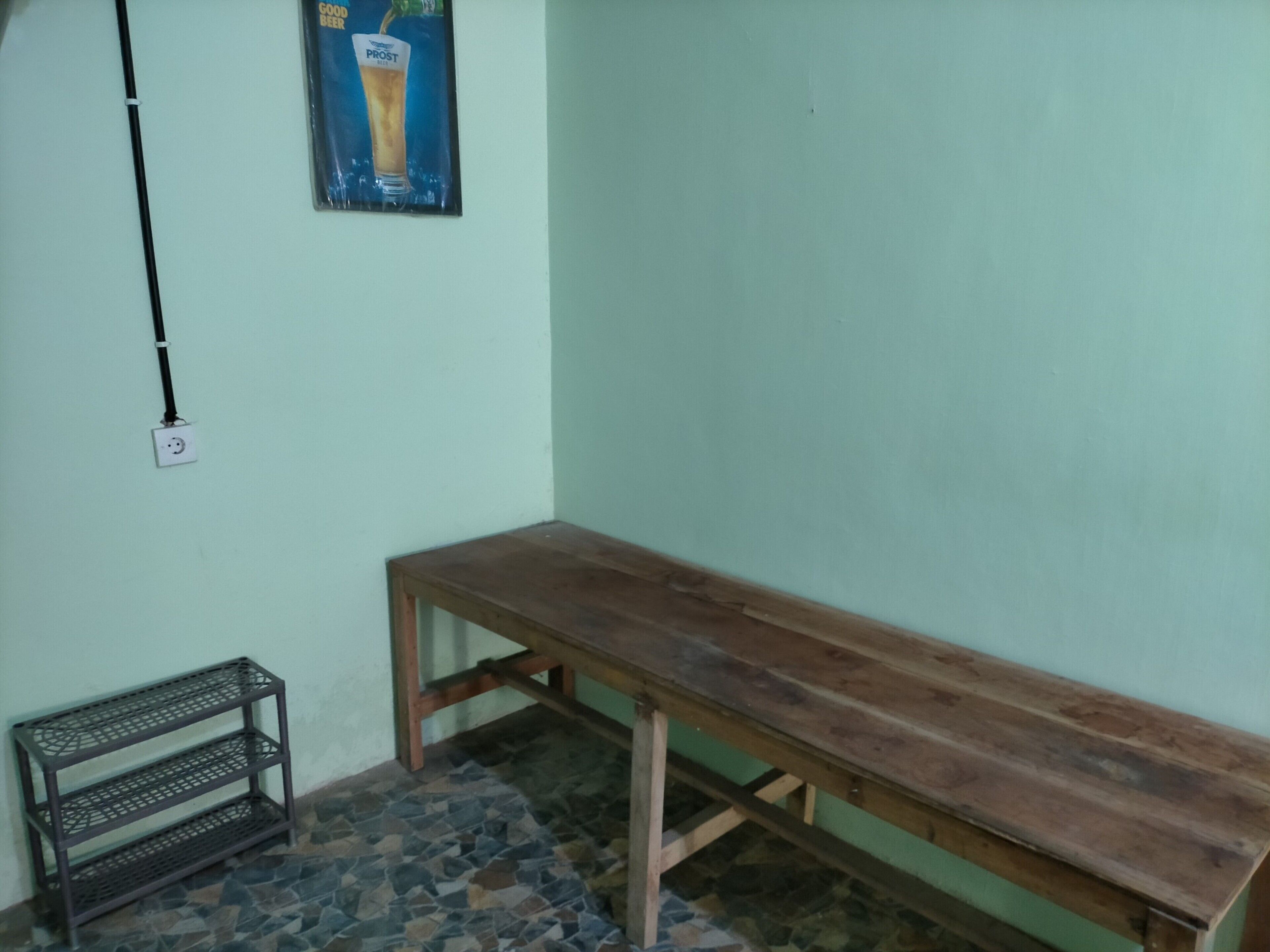 A room with a wooden bench, a metal shelf, and a wall-mounted electrical outlet.