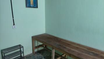A room with a wooden bench, a metal shelf, and a wall-mounted electrical outlet.