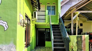 A green building with a staircase leading to a door, a window, and an air conditioning unit. - Gandrung City Hostel (Banyuwangi)