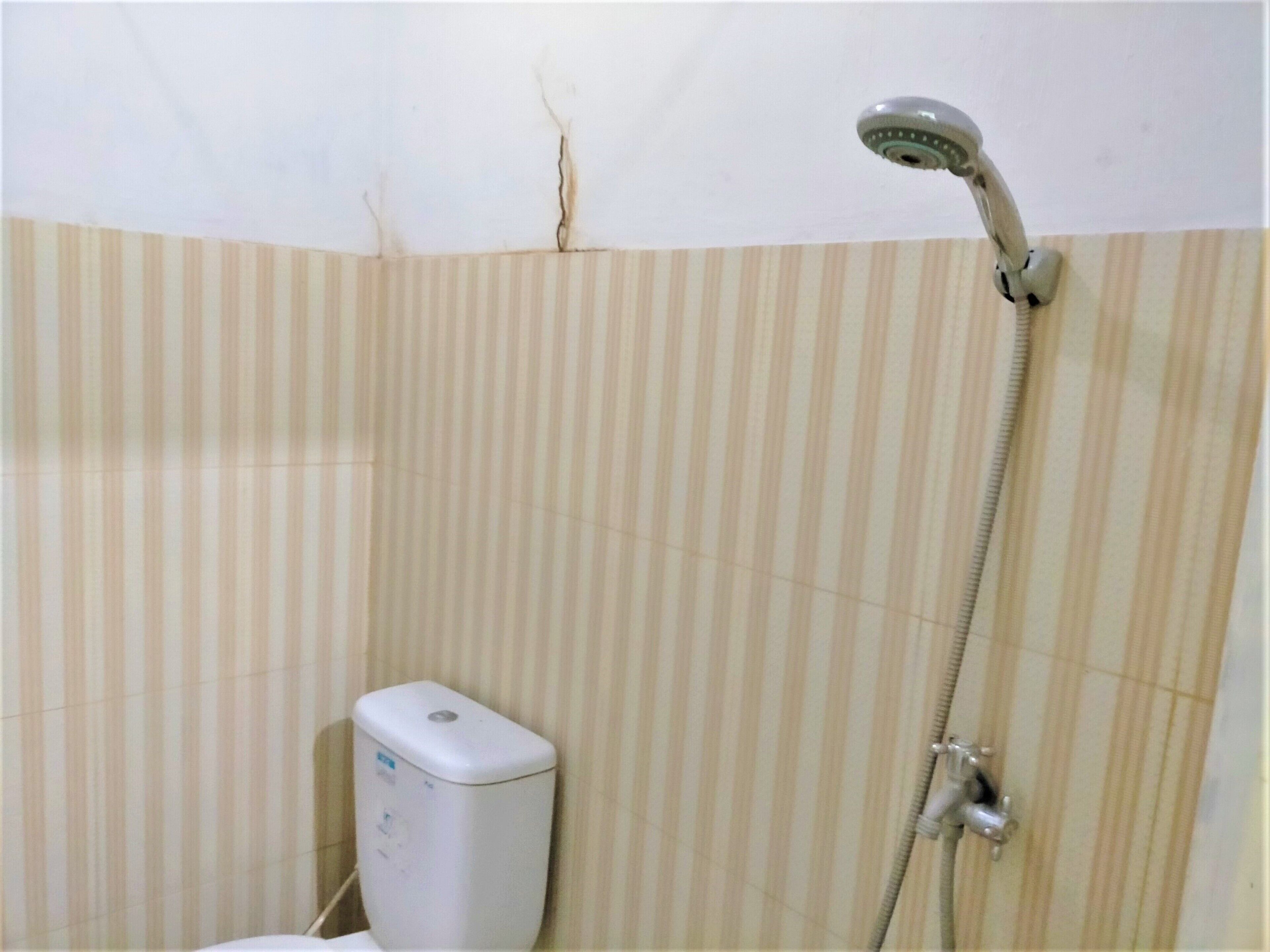 A bathroom with striped beige tiles, a handheld showerhead, and a white soap dispenser.