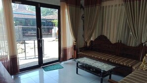 A room with a sofa, a coffee table, and a view through a glass door to the outside. - Gandrung City Hostel (Banyuwangi)