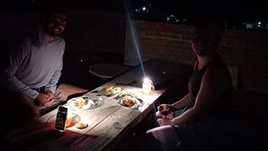 A wooden table with plates of food and a lit candle, suggesting an outdoor dining setting. - Gandrung City Hostel (Banyuwangi)