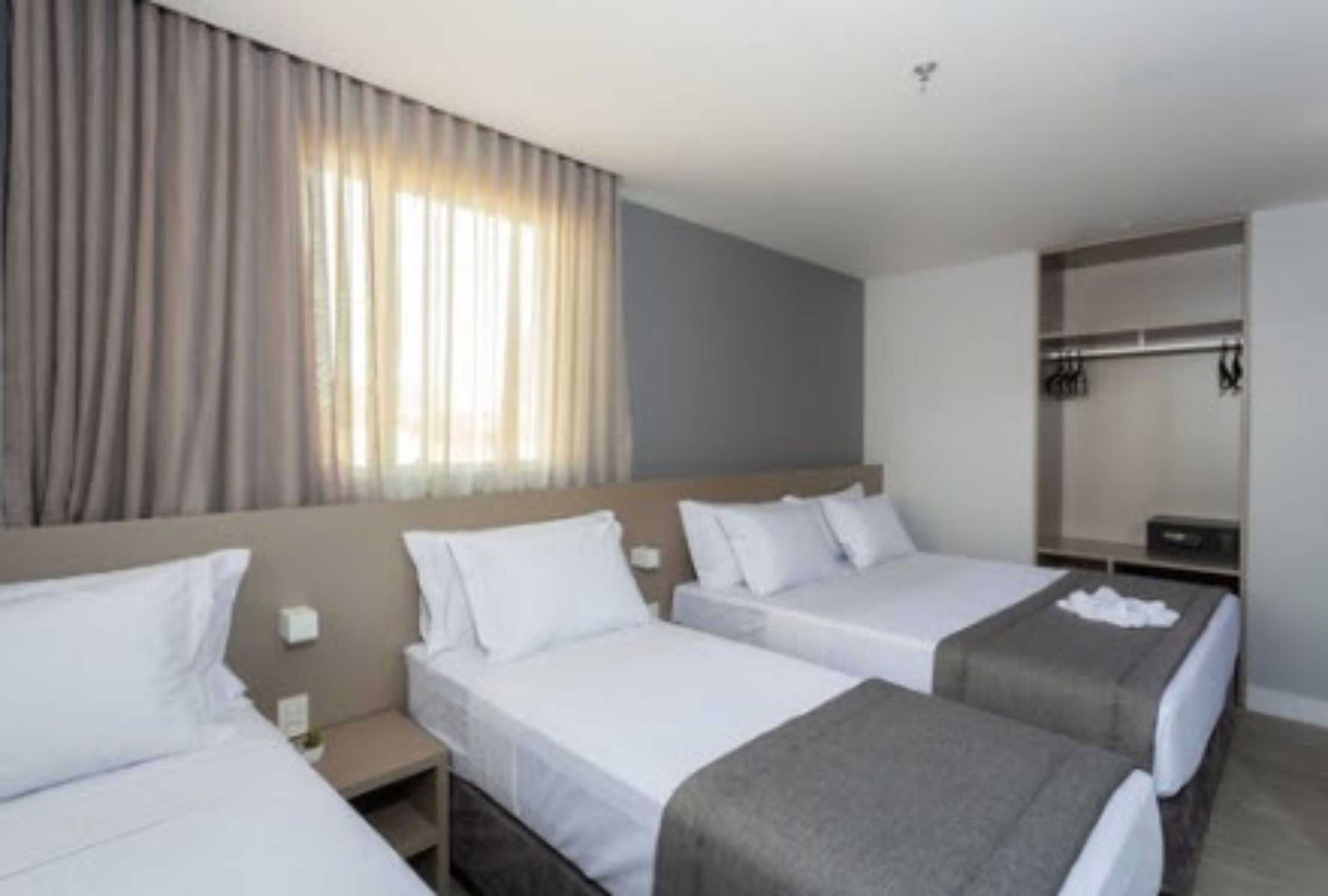 Una habitación de hotel con tres camas individuales, un armario y un ventanal con cortinas.