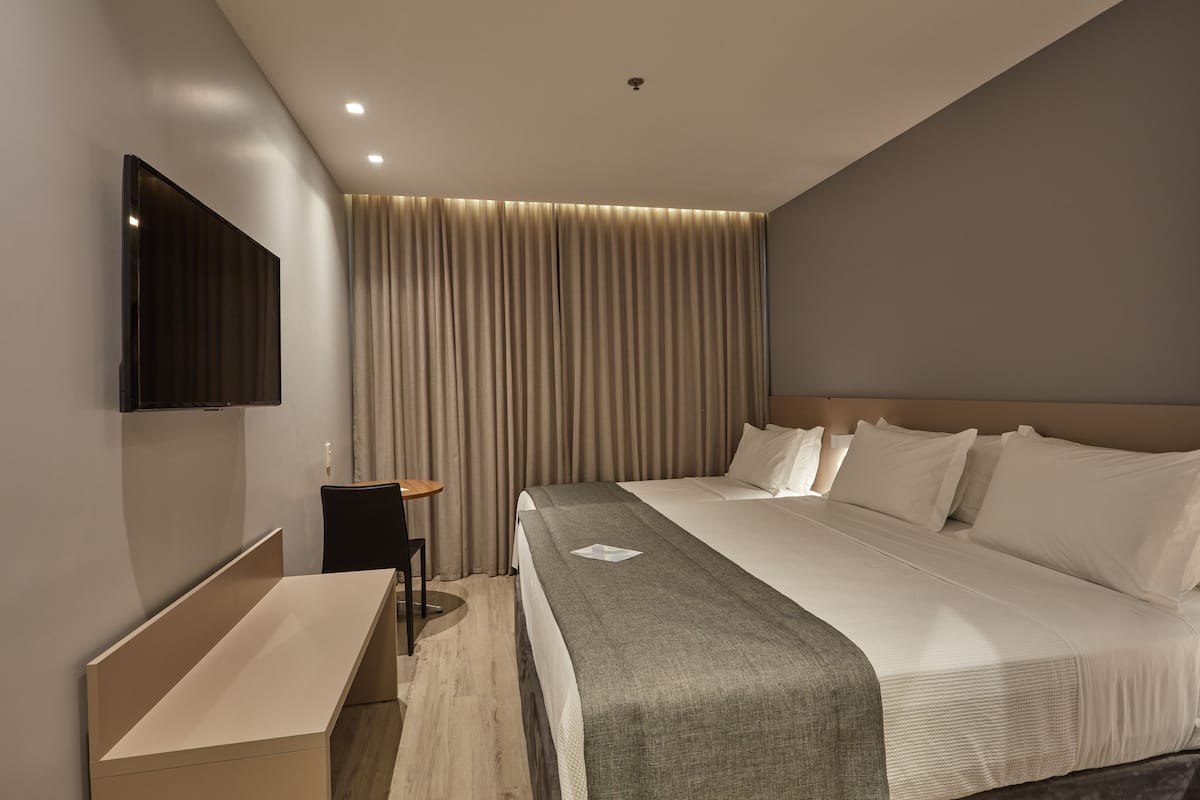 Una habitación de hotel moderna con una cama grande, un televisor de pantalla plana en la pared, un escritorio y una silla.
