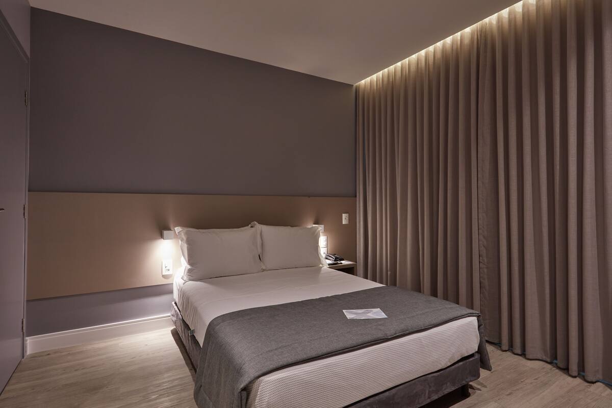 Una habitación de hotel moderna con una cama grande, una mesita de noche y una lámpara de pared.