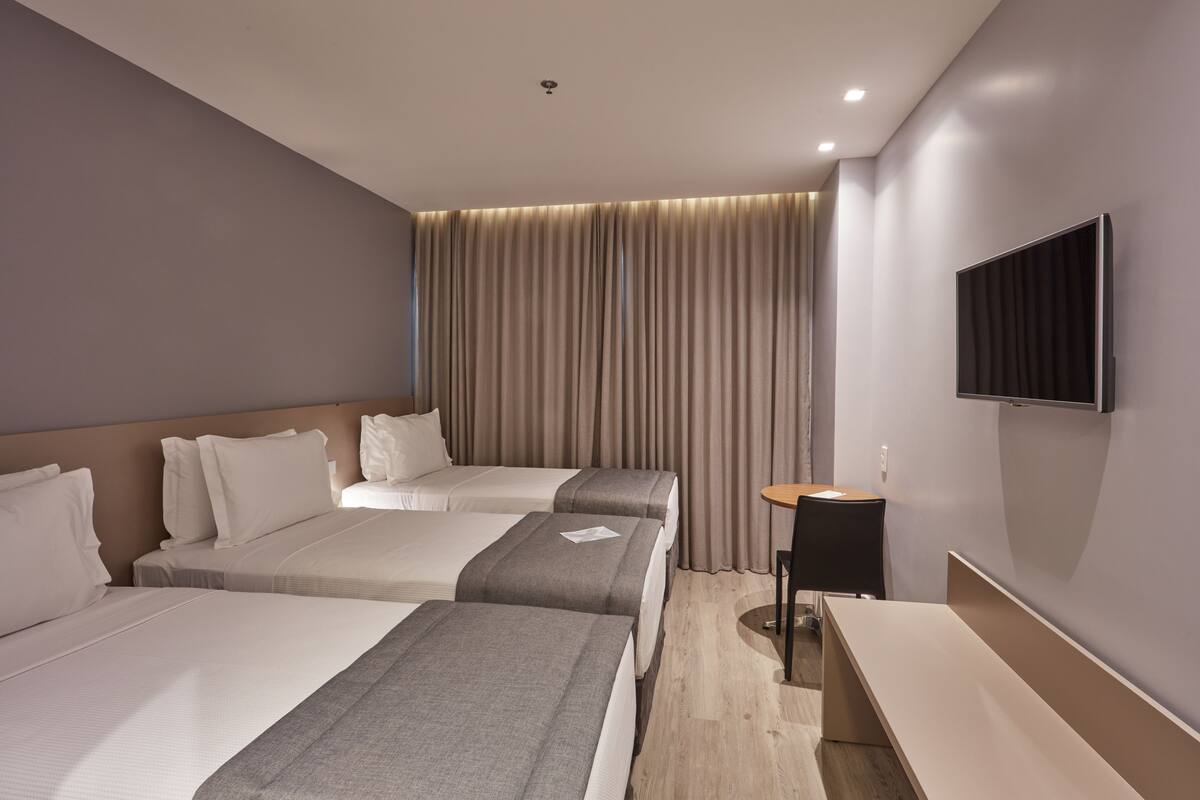 Habitación de hotel con dos camas, un televisor de pantalla plana, un escritorio y una ventana con cortinas.