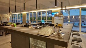 A modern bar area with a long counter, hanging pendant lights, and a large window providing a view of the outdoors. - Flix Hotel (Maceió)
