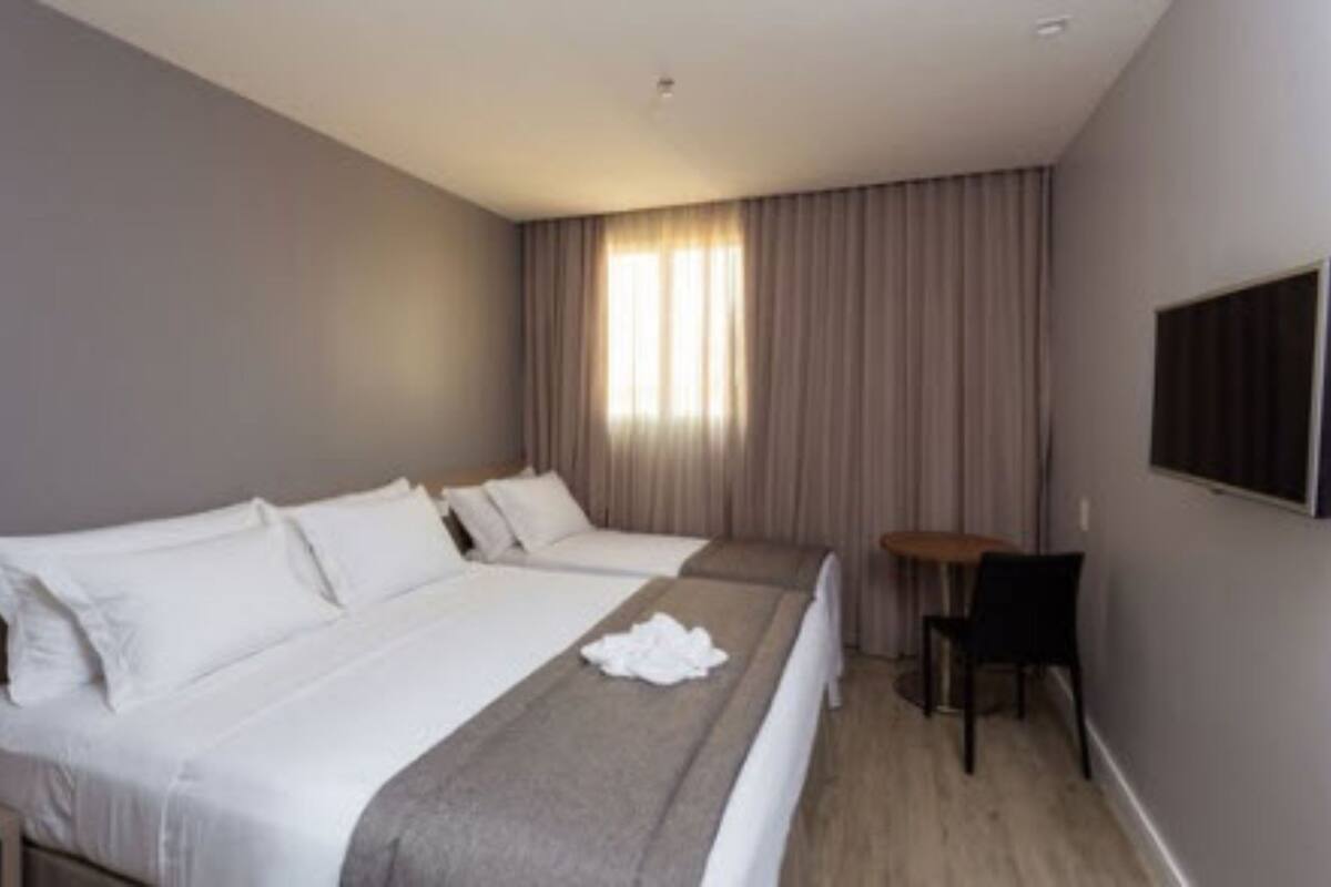 Habitación de hotel con dos camas, una mesita, una silla y un televisor en la pared.