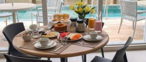 A breakfast table set with various dishes, a coffee pot, and a vase with yellow flowers.