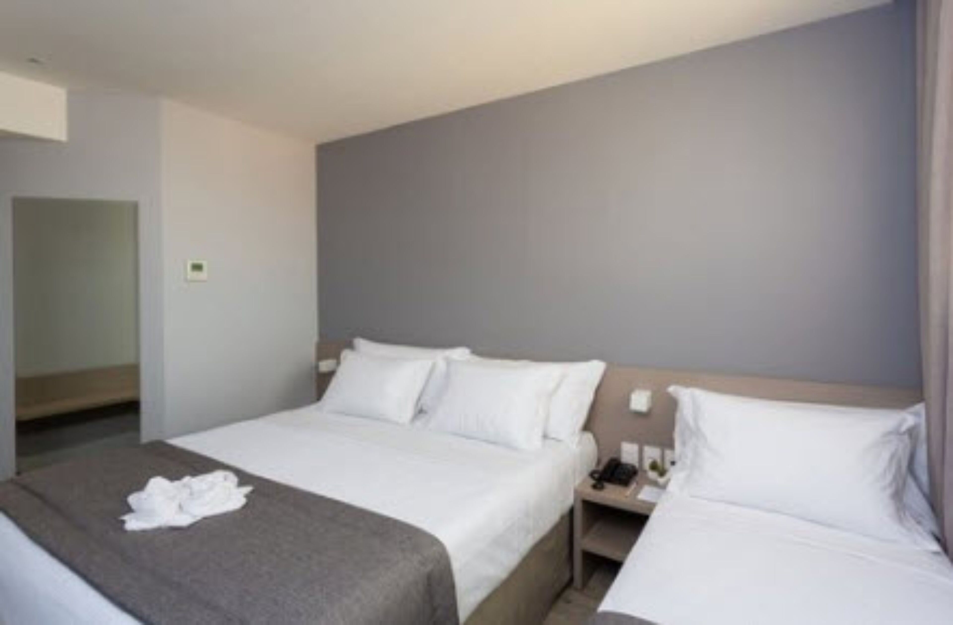 A hotel room with two beds, a bedside table with a phone, and a wall-mounted light.