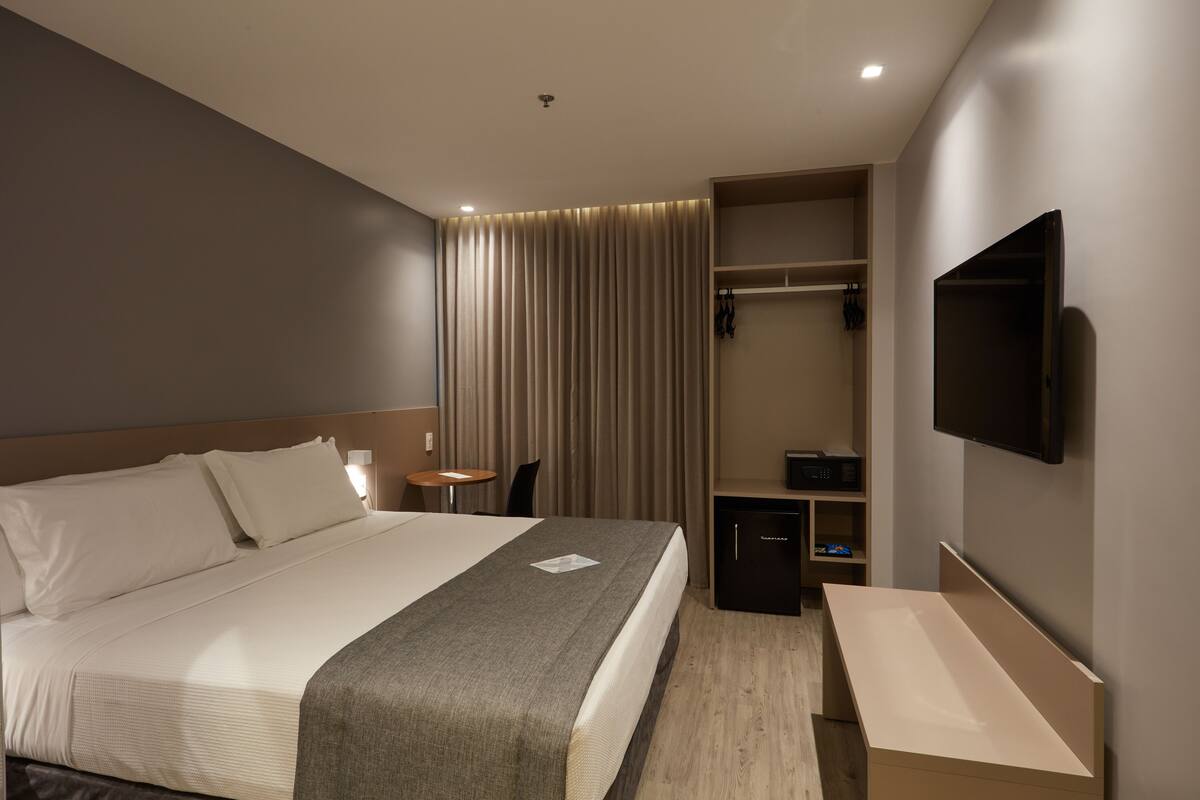 Una habitación de hotel moderna con una cama grande, un escritorio, un televisor y un armario.