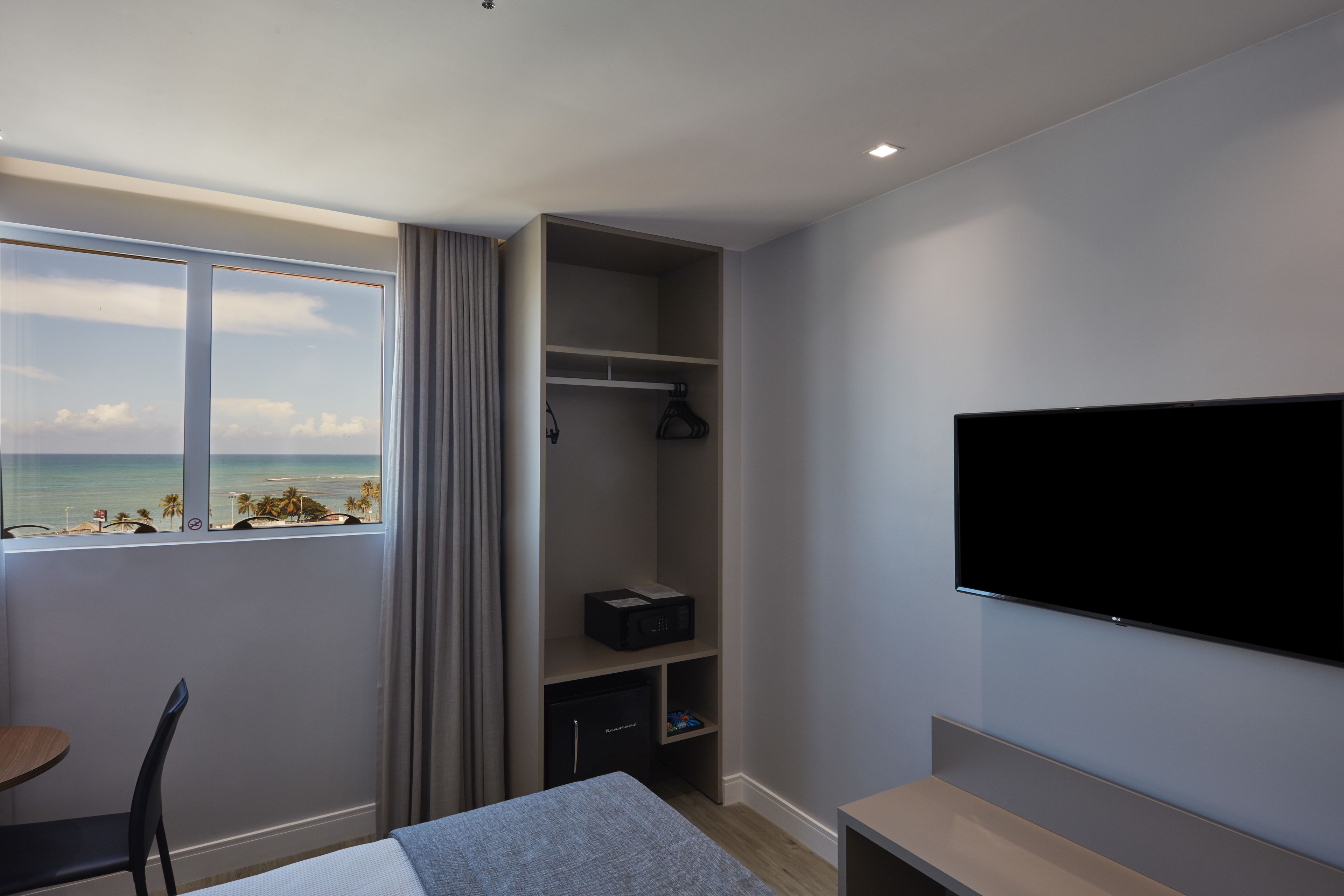 Habitación de hotel con cama, televisión, escritorio y ventana con vista a la playa.
