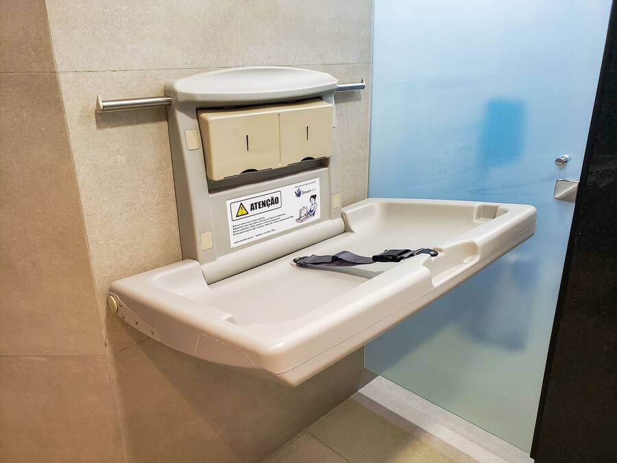 A portable toilet with a safety warning label, a metal grab bar, and a plastic seat.
