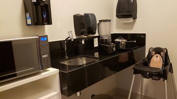 Uma cozinha compacta equipada com micro-ondas, cafeteira e bebedouro.