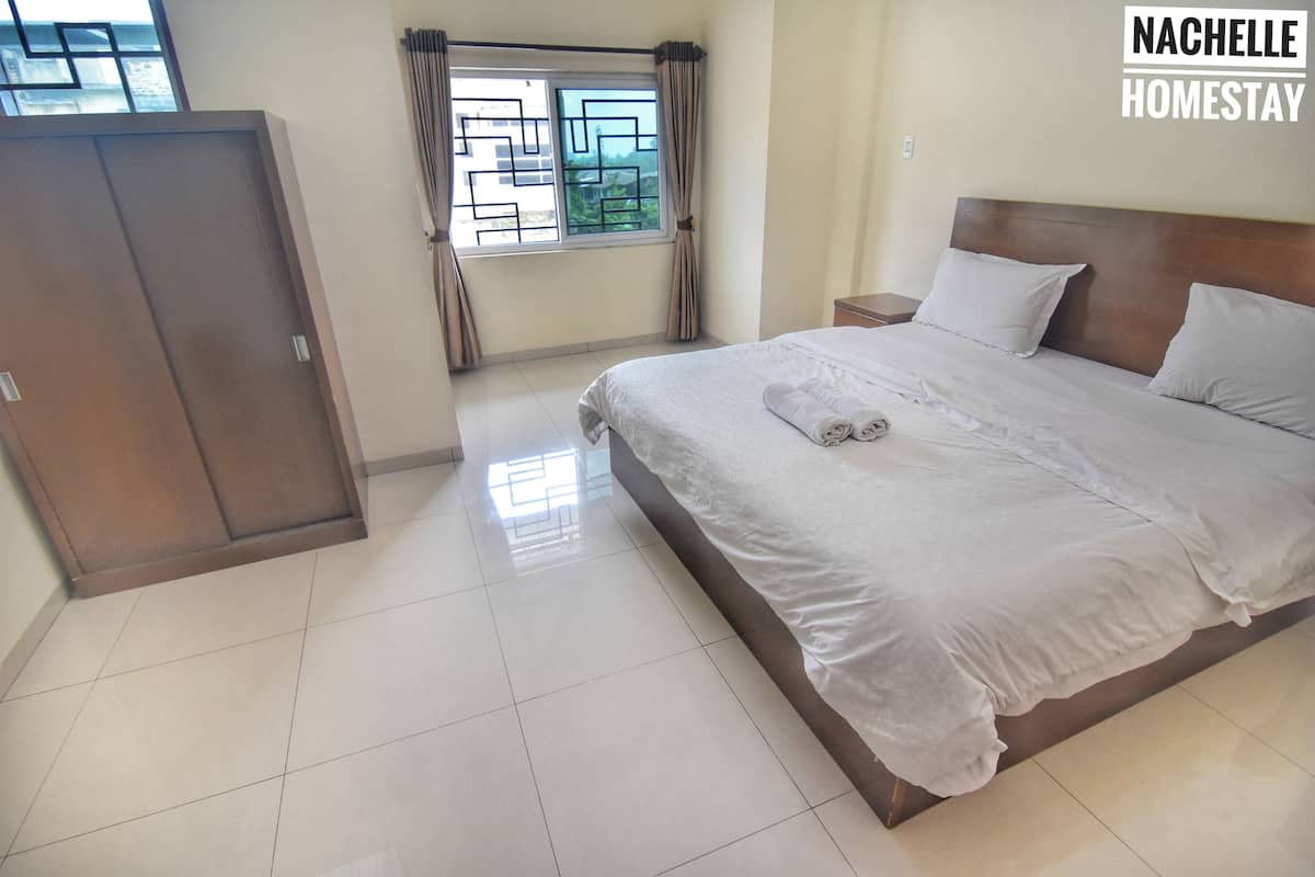 A bedroom with a large bed, a wardrobe, and a window with curtains.
