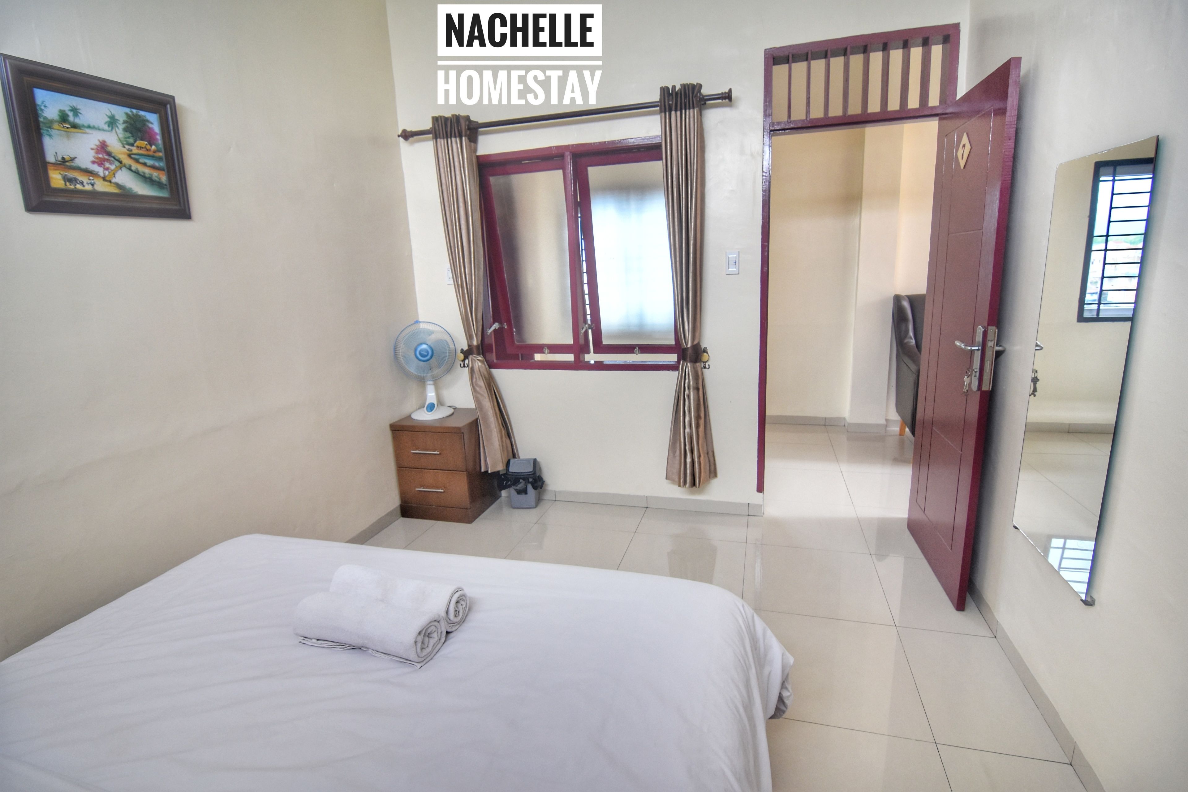 Una habitación de hotel con cama, mesita de noche, ventana con cortinas, puerta y televisor instalado en la pared.